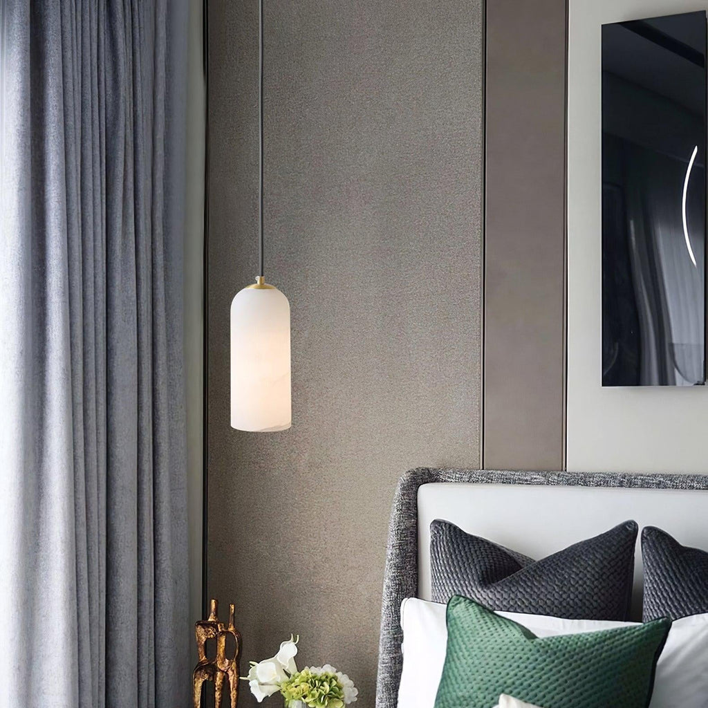 Hecate pendant hung as a bedside light beside a grey upholstered headboard and green cushions.