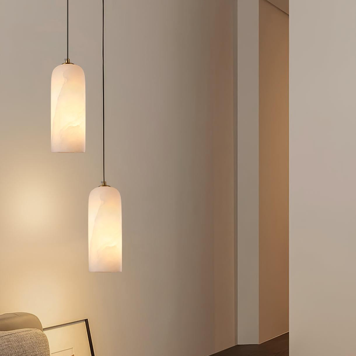 Two Hecate pendants hung at different drops in a pale corner, casting warm light down the wall.