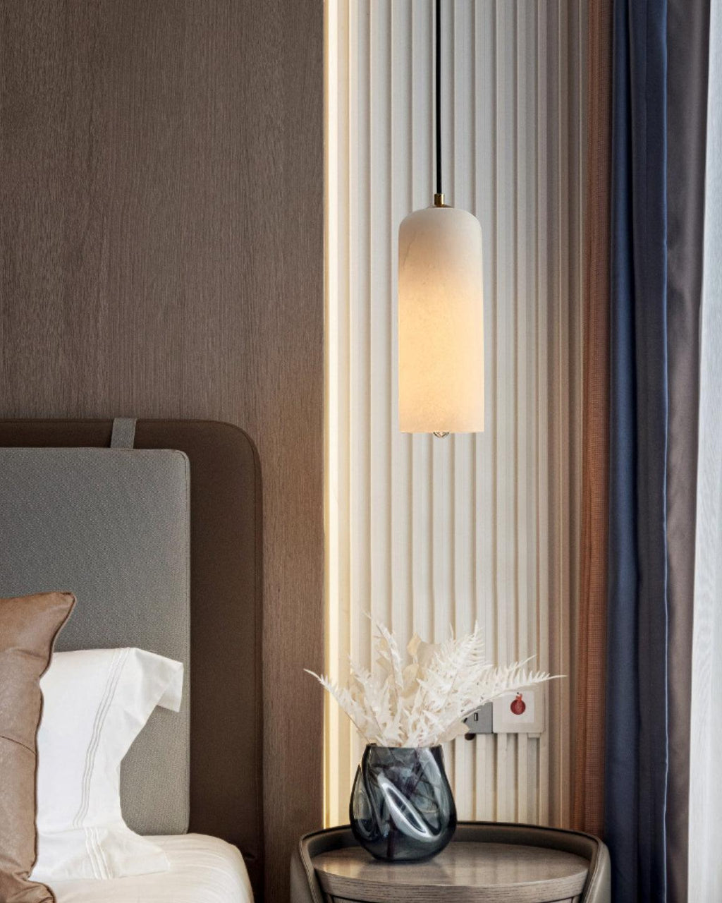 Zashayra pendant beside a fluted wall panel and a bedside table holding a blue glass vase.