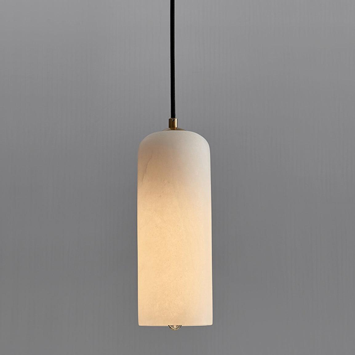 Zashayra alabaster pendant light hanging against a grey wall, its cylindrical shade lit to a soft cream glow.