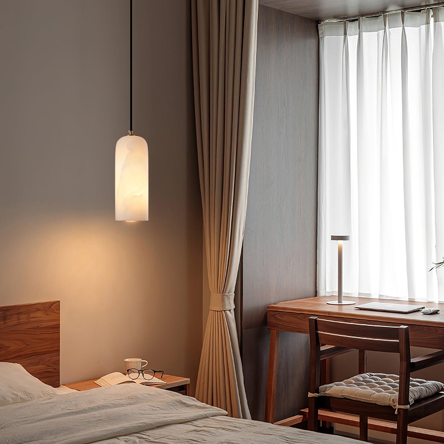 Hecate pendant hung low beside a wooden bed, lighting a book and mug in a curtained bedroom.