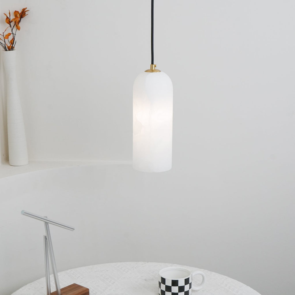 The Zashayra pendant over a round table set with a checkered mug and a slim metal sculpture.