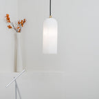 Hecate pendant glowing beside a slim white vase of dried orange stems in a bright corner.