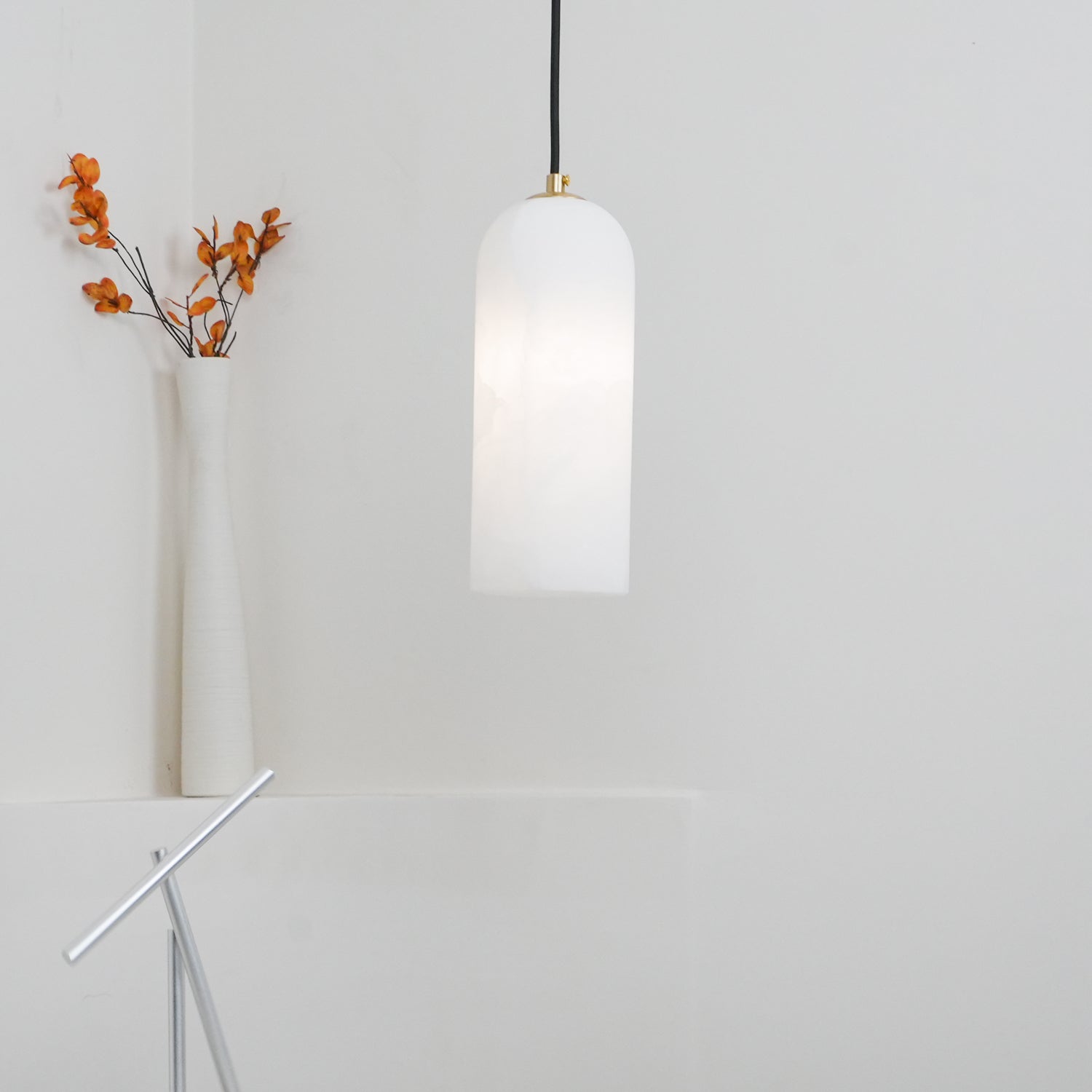 Hecate pendant glowing beside a slim white vase of dried orange stems in a bright corner.