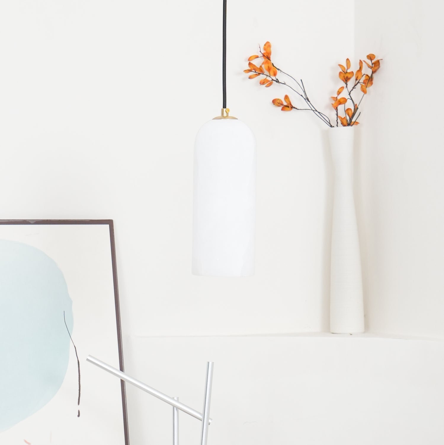 The unlit Zashayra pendant in a white styled corner beside a tall vase of dried orange branches.