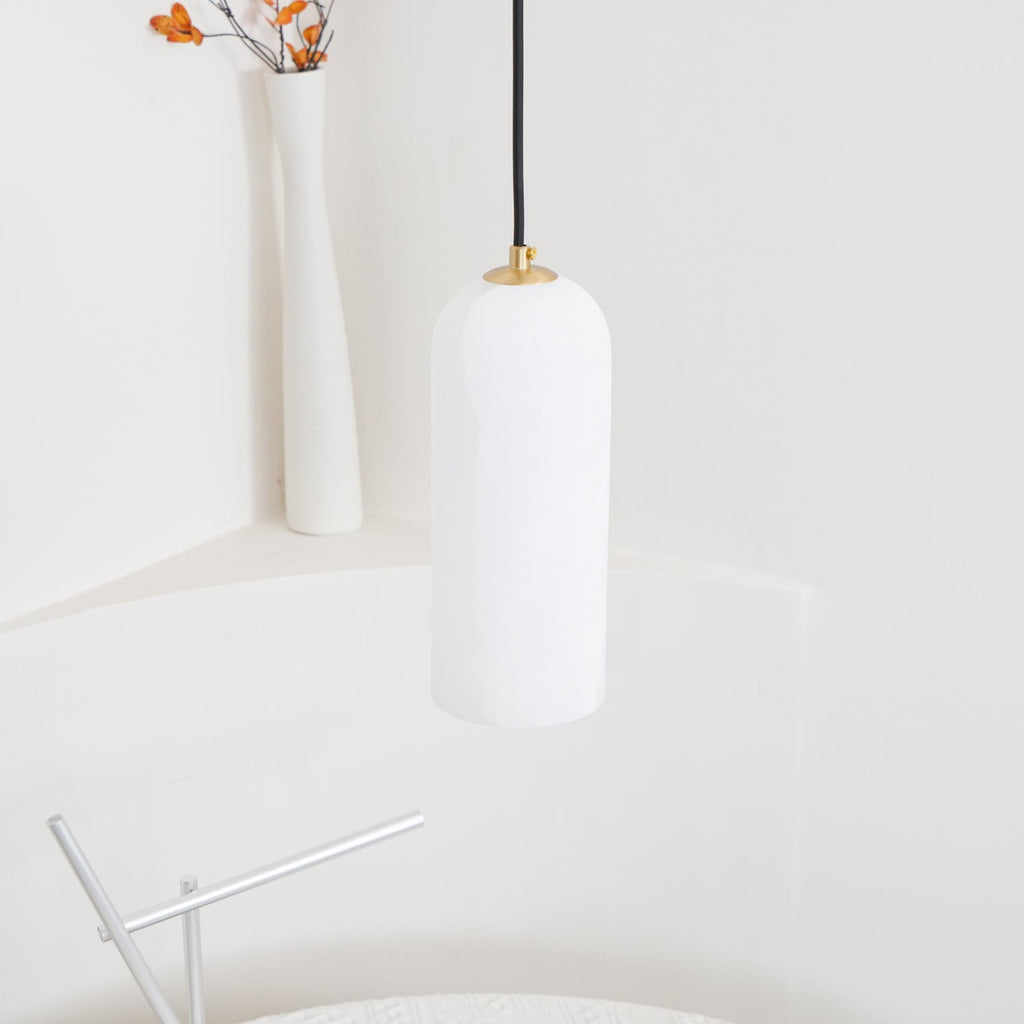 Zashayra pendant hanging above a round white table beside a slim ribbed ceramic vase.