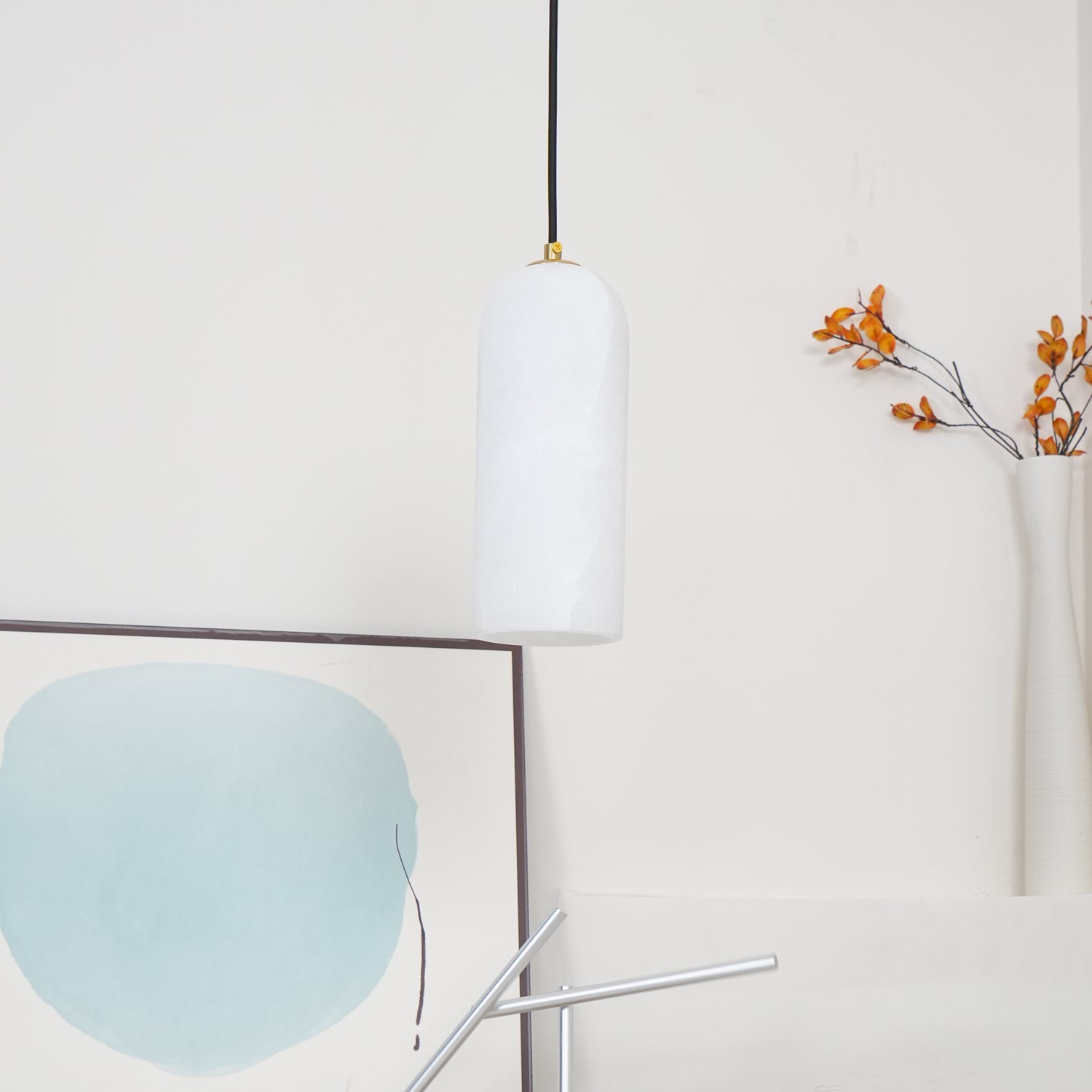 The unlit Zashayra pendant beside a framed blue abstract print, the alabaster reading cool white.
