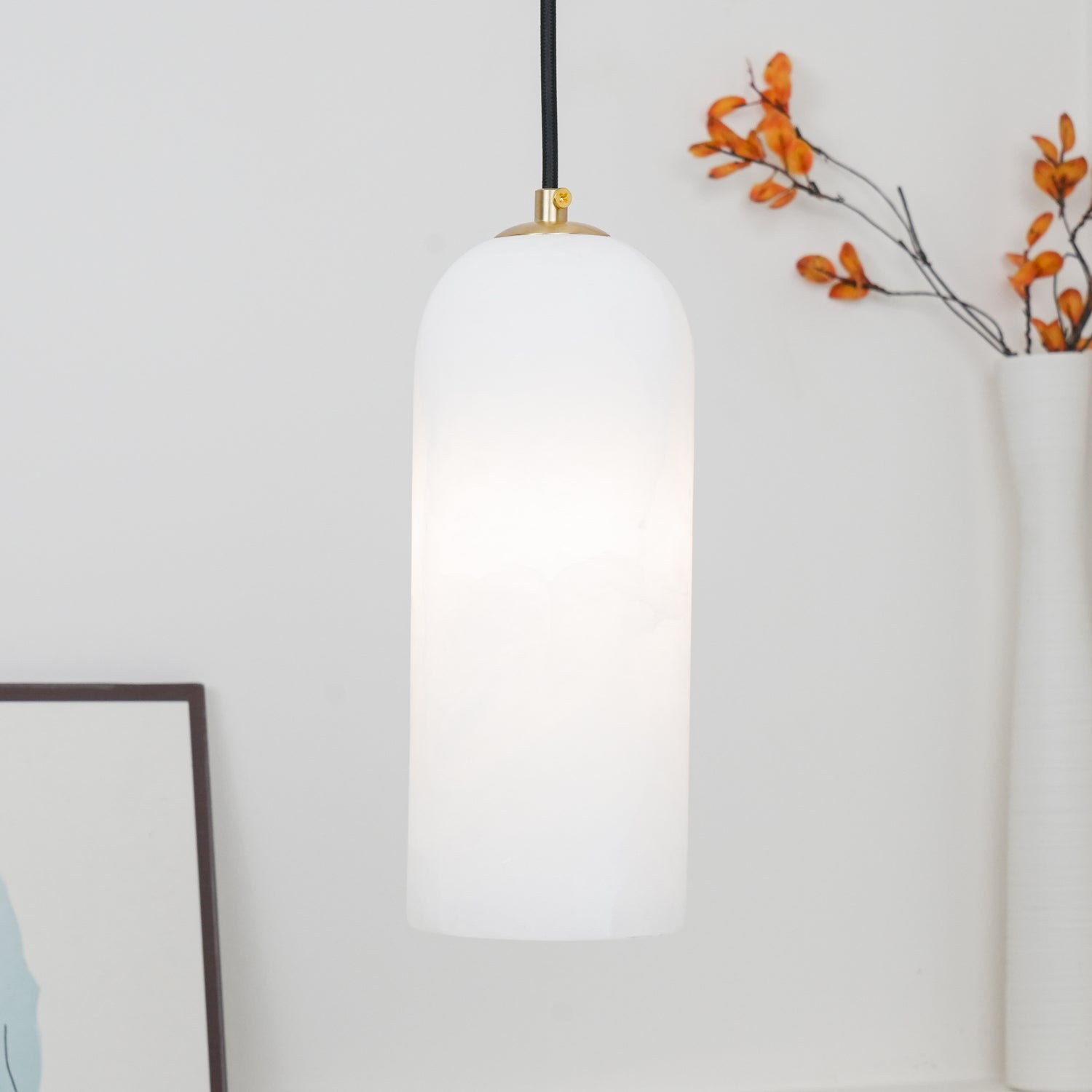 Zashayra pendant glowing between a framed print and a vase of autumn branches.