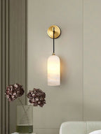Vaelara alabaster sconce lit on a greige panelled wall beside dried hydrangeas in a ribbed vase