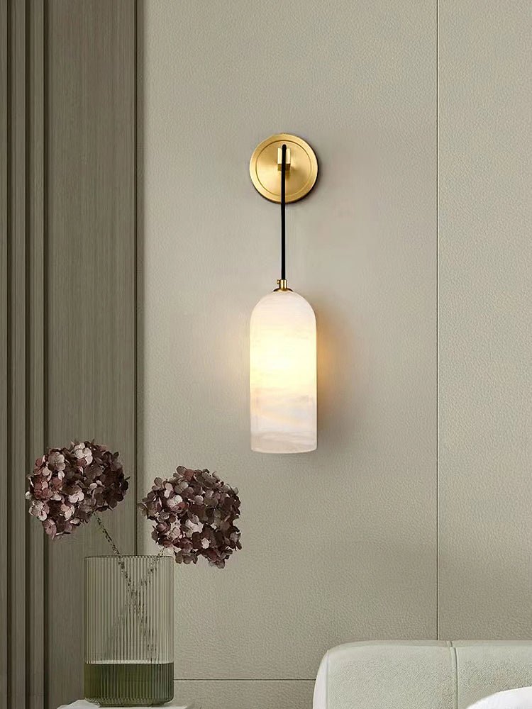 Vaelara alabaster sconce lit on a greige panelled wall beside dried hydrangeas in a ribbed vase