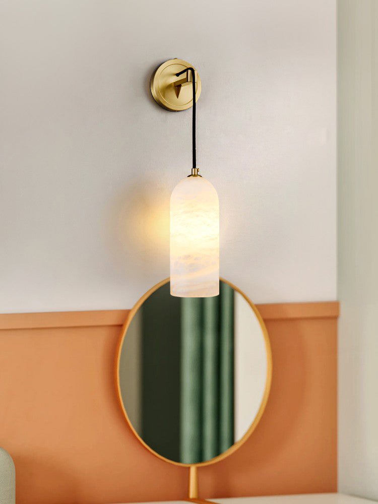 Vaelara sconce lit above a round gold-framed vanity mirror on a wall with terracotta wainscoting