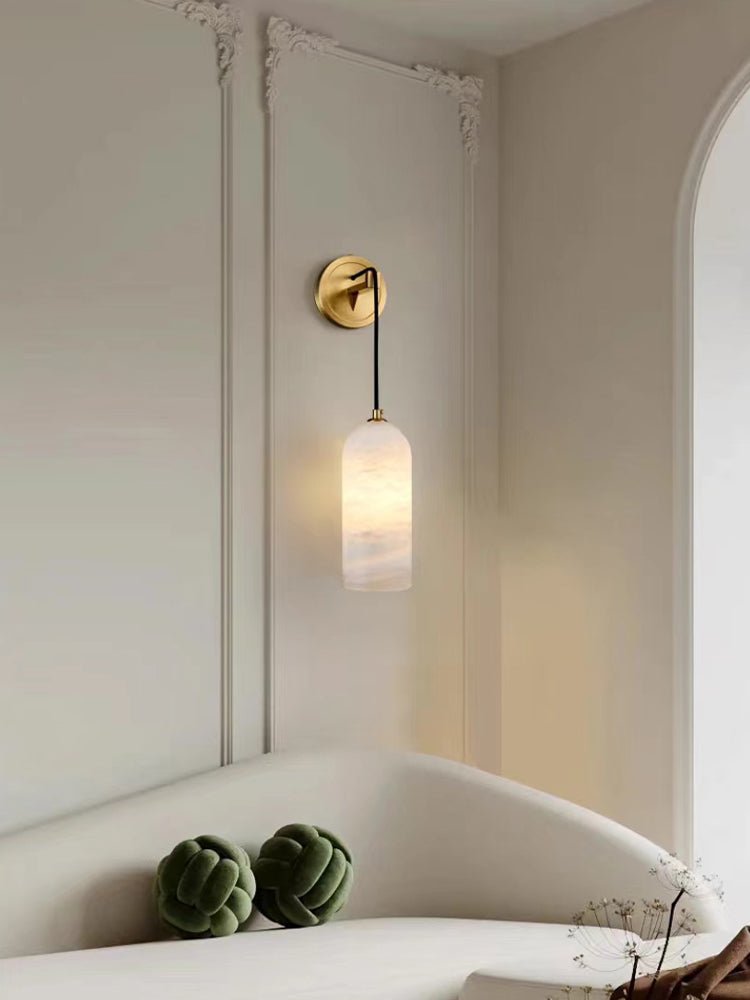 Vaelara sconce lit on ornate cream wall panelling above a curved sofa with green knot cushions