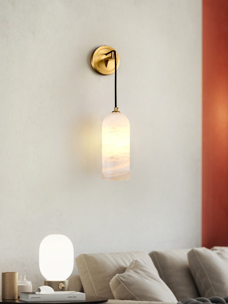 Vaelara sconce lit on a pale wall beside a rust-red panel, above a beige sofa and a round table lamp