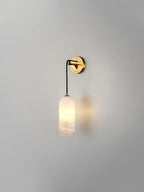 Vaelara sconce lit on a plain grey wall, its warm glow pooling on the plaster beside the shade