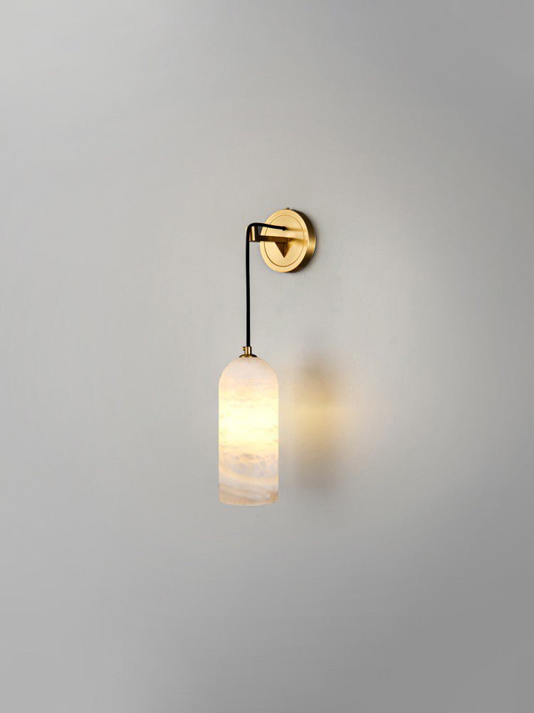 Vaelara sconce lit on a plain grey wall, its warm glow pooling on the plaster beside the shade