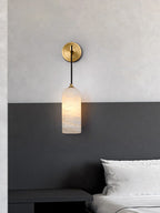Vaelara sconce lit above a black nightstand, mounted where the pale wall meets a dark grey panel