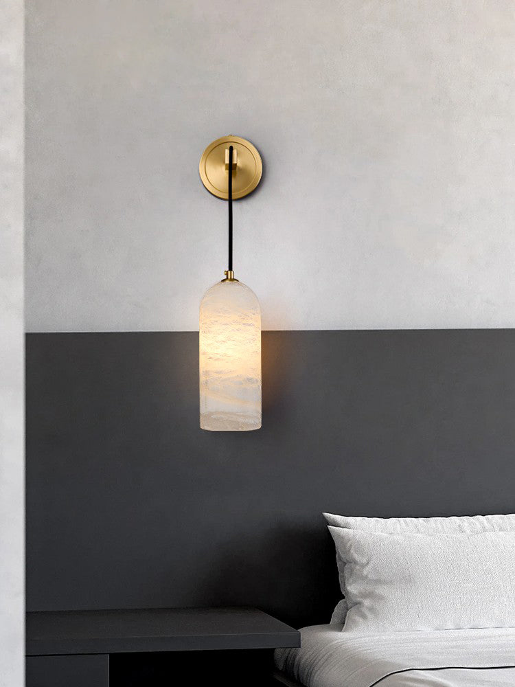 Vaelara sconce lit above a black nightstand, mounted where the pale wall meets a dark grey panel