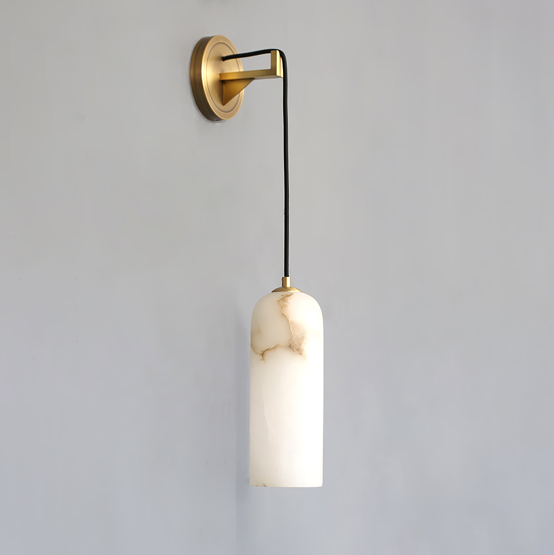 Side view of the Vaelara wall sconce unlit, the brass arm angling the cord out from the wall plate