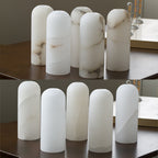 Ten unlit alabaster shades lined up on a dark table, showing how the natural veining varies