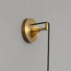Detail of the brushed brass wall plate and angled bracket that carries the sconce's black cord