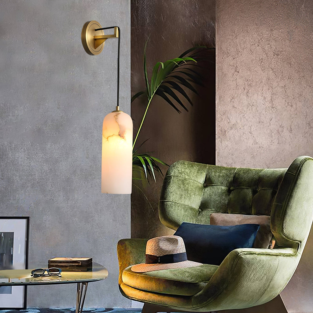 Vaelara sconce lit above a glass side table beside a green velvet armchair and potted palm