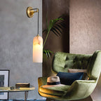 Vaelara sconce lit above a glass side table beside a green velvet armchair and potted palm