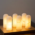 Six alabaster shades lit side by side on a brass tray, each stone glowing a slightly different pattern