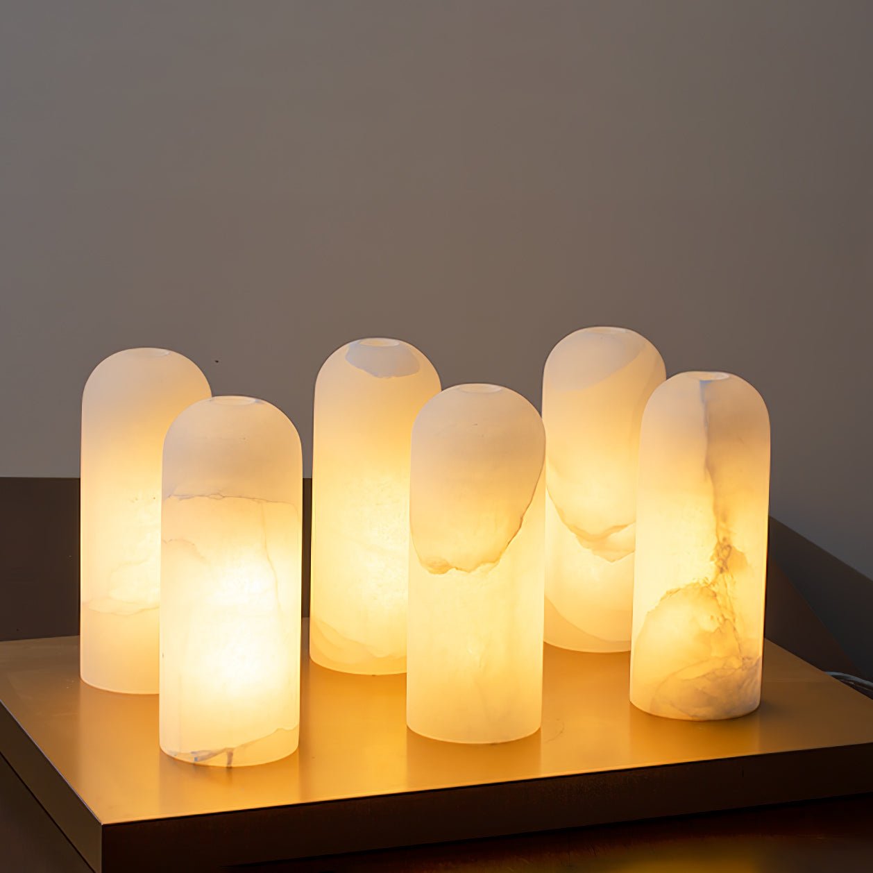 Six alabaster shades lit side by side on a brass tray, each stone glowing a slightly different pattern