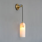 Vaelara alabaster wall sconce with a long cord drop, lit shade hanging well below the brass arm