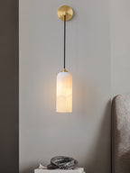 Vaelara alabaster sconce lit beside a bed, its glow washing the grey wall above a marble sculpture