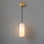 Vaelara sconce viewed head-on, the round brass wall plate and straight black cord above the lit shade