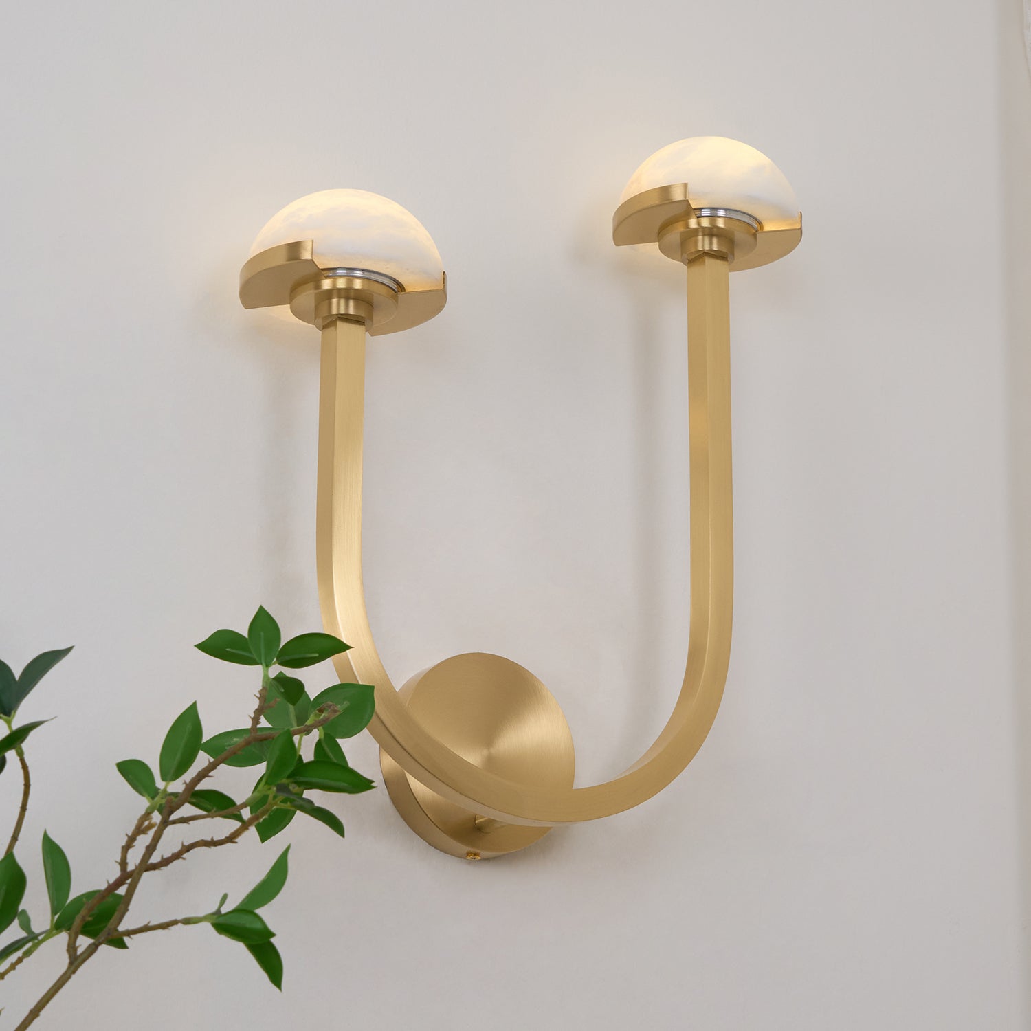 Brass Vitalira Double Alabaster Wall Light lit head-on, its two arms sweeping into a wide U.