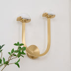 Brass Vitalira Double Alabaster Wall Light on a white wall, viewed from below with a plant in frame.