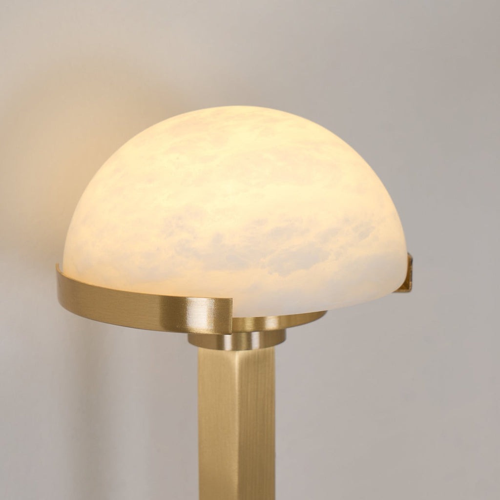 Close-up of a single lit alabaster dome cradled in the brushed brass collar of the Vitalira wall light.