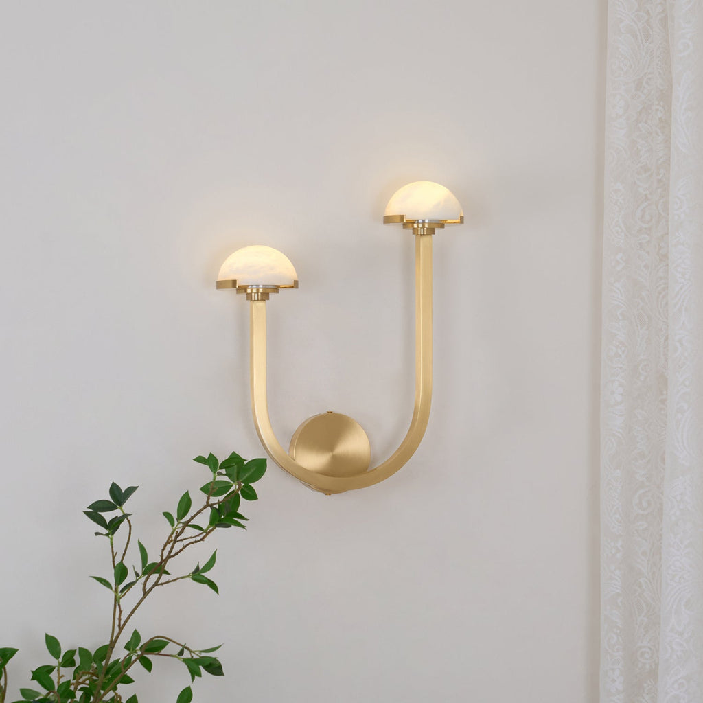 Brass Vitalira Double Alabaster Wall Light lit on a white wall, one dome set higher than the other.