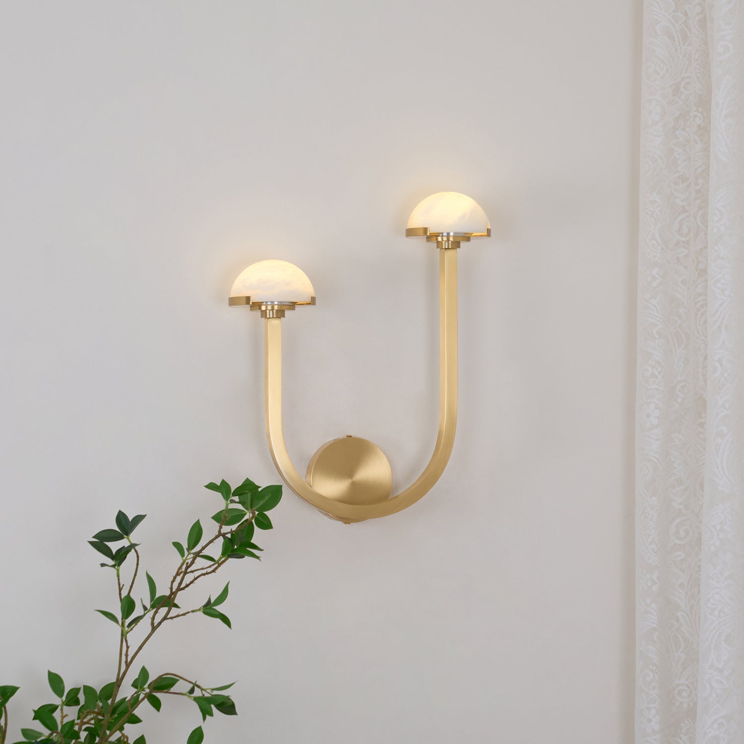 Brass Vitalira Double Alabaster Wall Light lit on a white wall, one dome set higher than the other.