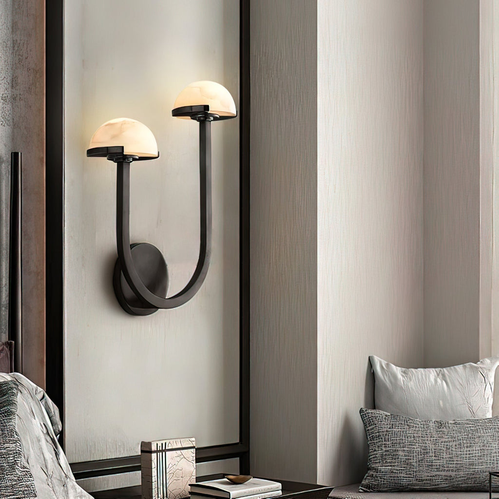 Black Vitalira Double Alabaster Wall Light lit on a pale panelled wall between two textured cushions.