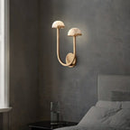 Brass Vitalira Double Alabaster Wall Light lit on a concrete-grey bedroom wall beside a window.