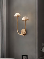 Brass Vitalira Double Alabaster Wall Light lit on a grey wall, framed picture and curtain nearby.