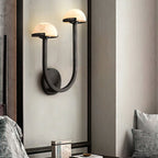 Vitalira Double Alabaster Wall Light in black lit on a panelled bedroom wall above a stack of books.