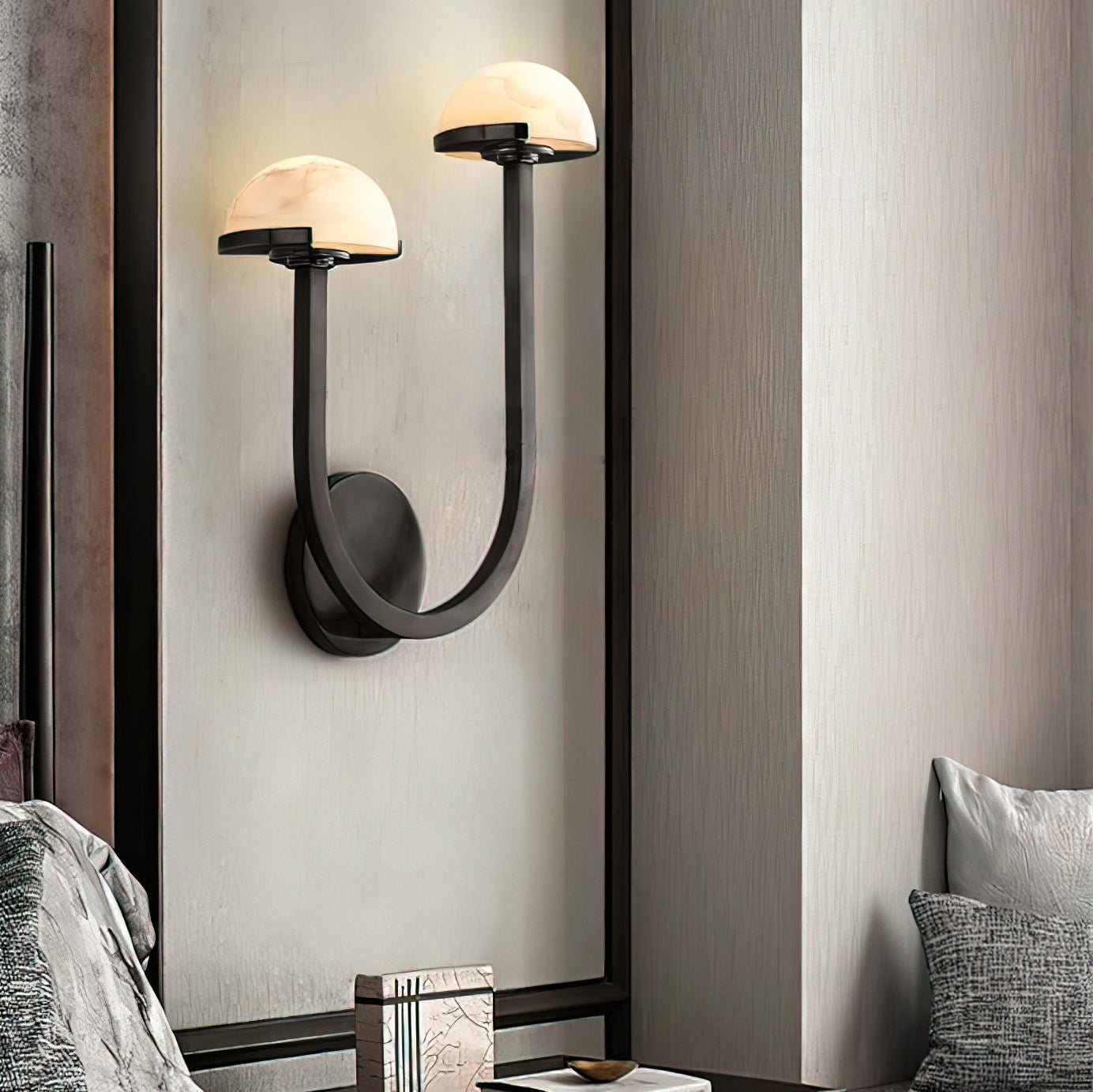Vitalira Double Alabaster Wall Light in black lit on a panelled bedroom wall above a stack of books.