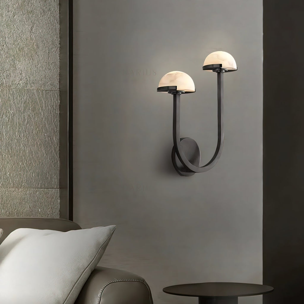 Vitalira Double Alabaster Wall Light in black lit beside a bed, casting a warm halo on the grey wall.