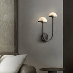 Vitalira Double Alabaster Wall Light in black lit beside a bed, casting a warm halo on the grey wall.
