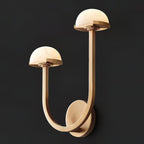 Brass Vitalira Double Alabaster Wall Light lit against a black backdrop, alabaster domes glowing warm.