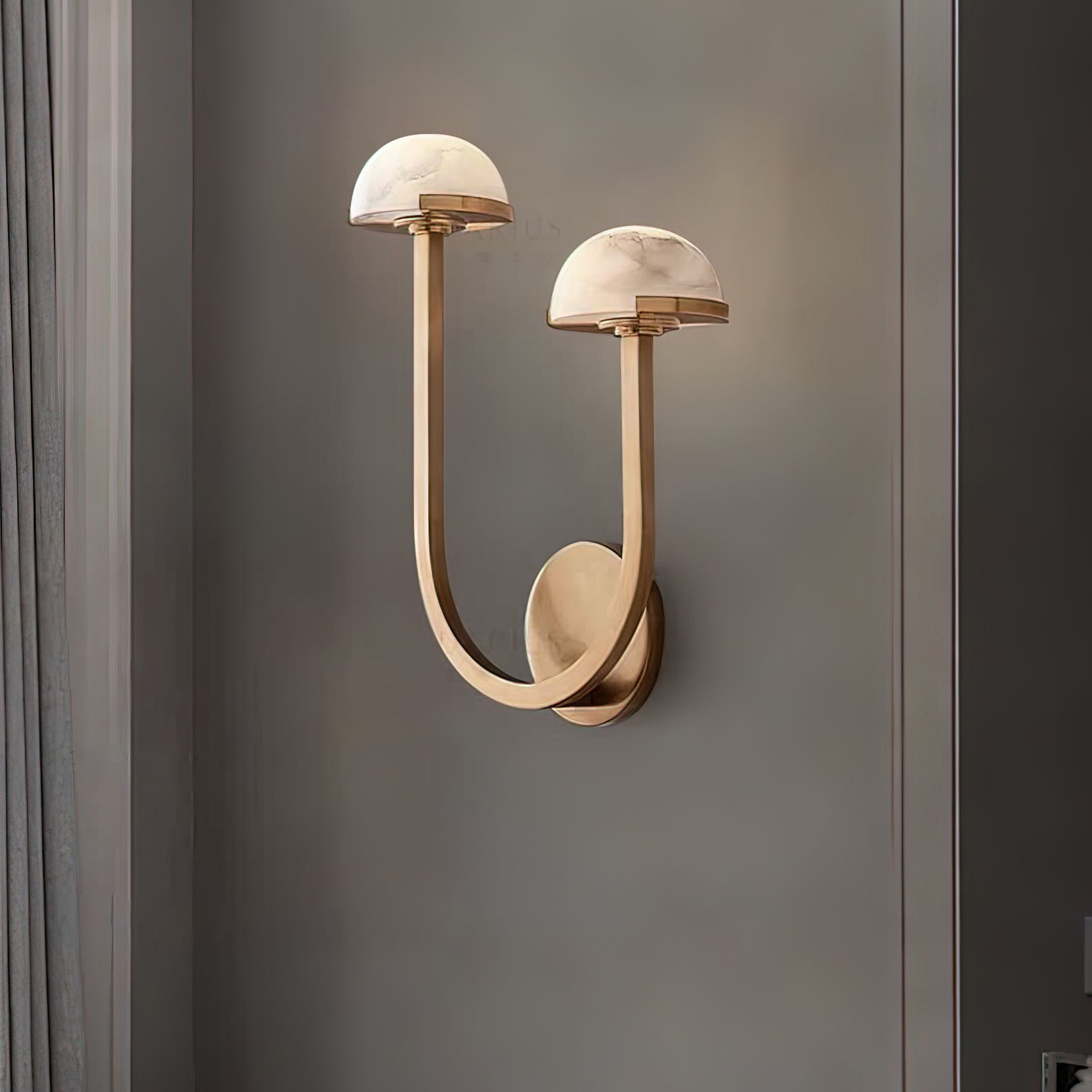 Brass Vitalira Double Alabaster Wall Light lit on a grey wall beside a painted window surround.