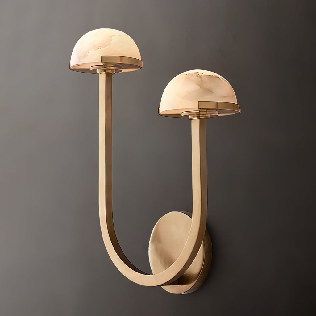 Brass Vitalira Double Alabaster Wall Light lit against a warm grey backdrop, arm curving from the plate.