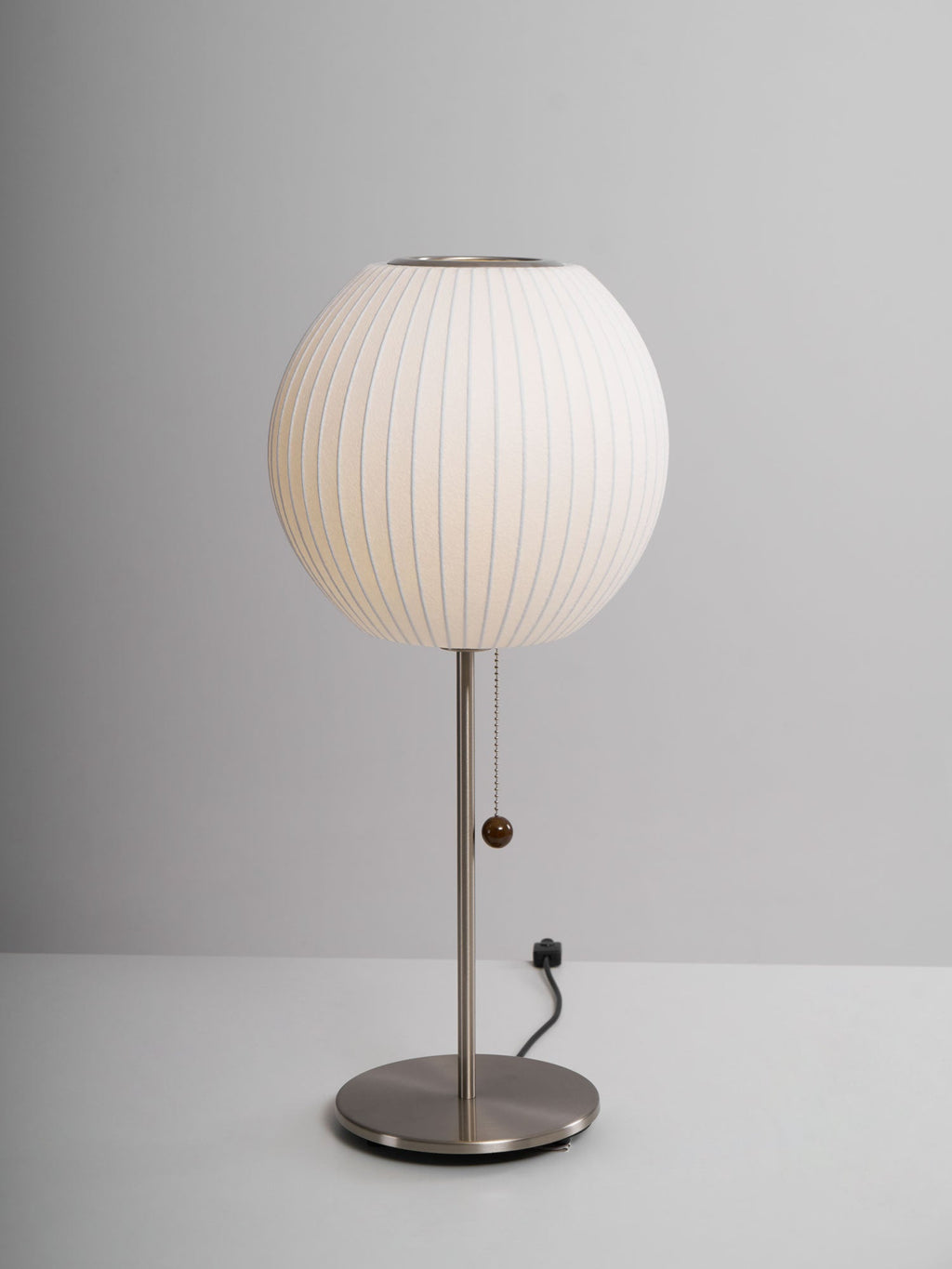 Faux silk bubble table lamp with chrome stem lit warmly on a side table
