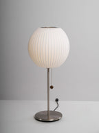Faux silk bubble table lamp with chrome stem lit warmly on a side table