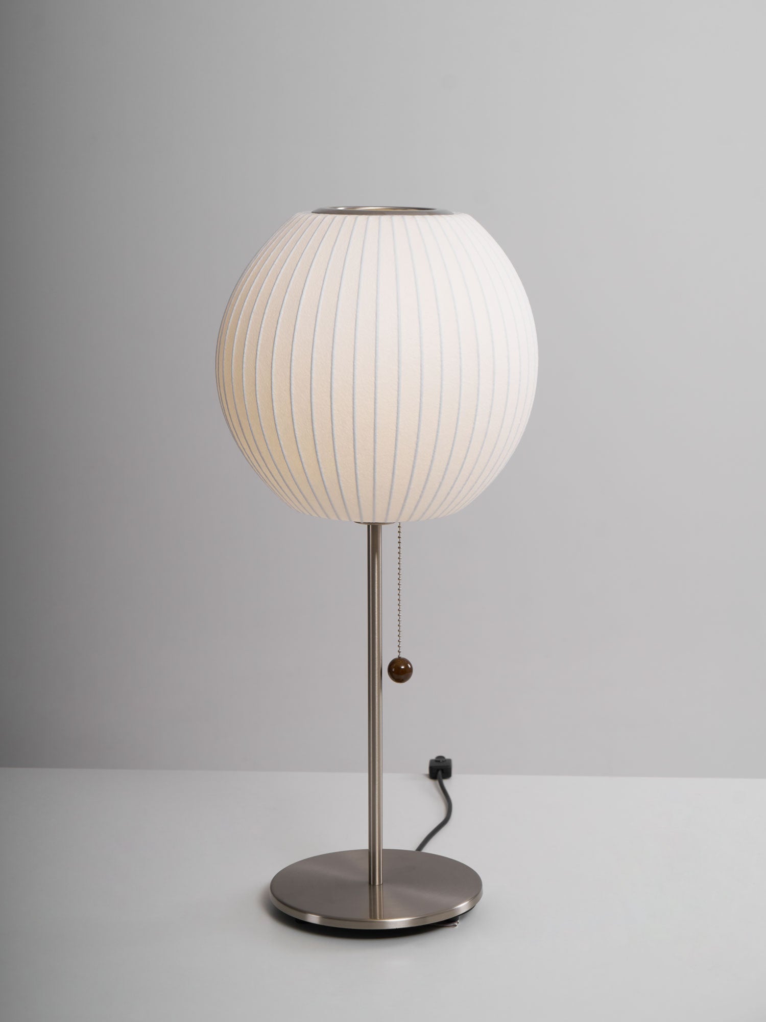 Faux silk bubble table lamp with chrome stem lit warmly on a side table