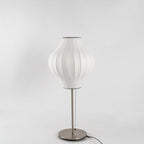 Faux silk bubble table lamp with chrome stem lit warmly on a side table